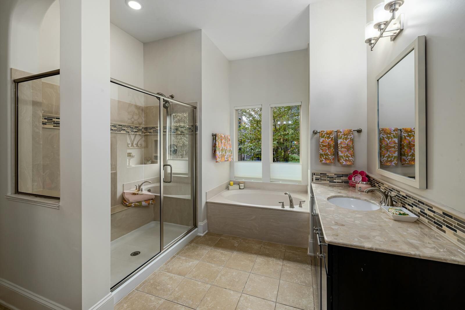 A contemporary bathroom featuring a bathtub, shower, vanity, and natural light through windows.