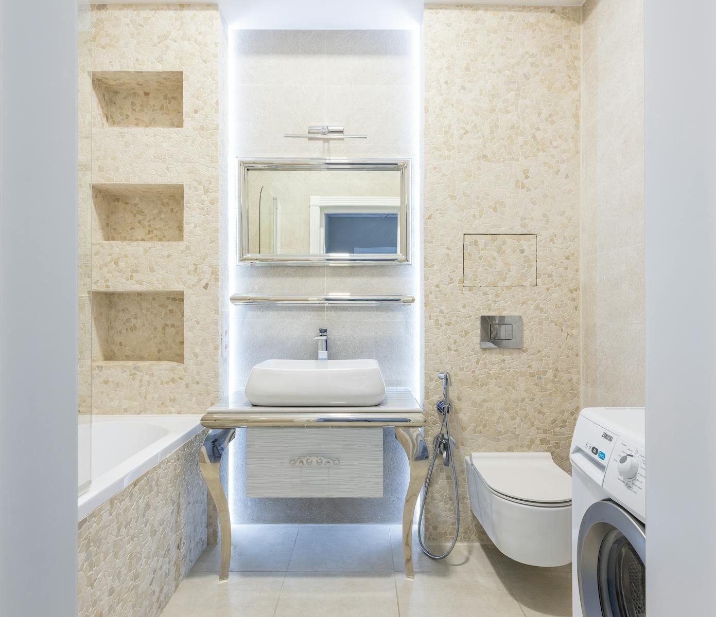 Bright, modern bathroom with beige tiles, washing machine, and elegant fixtures.