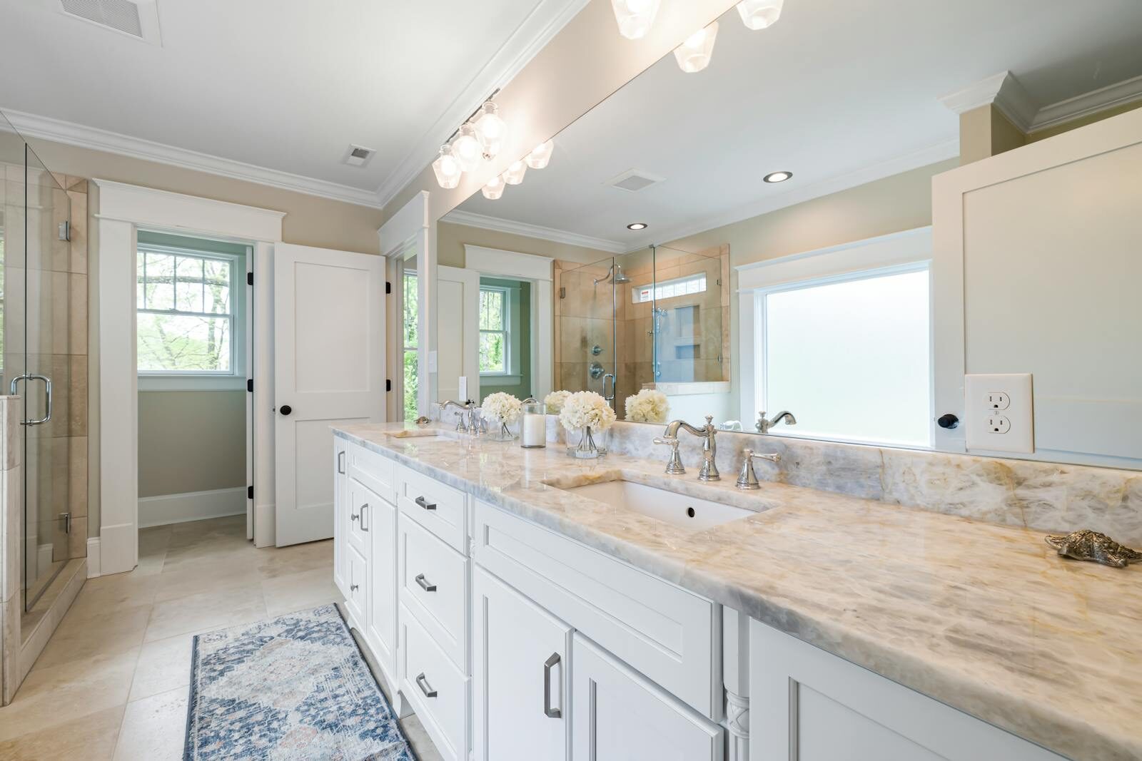 Spacious bathroom with marble countertop, glass shower, and elegant lighting.