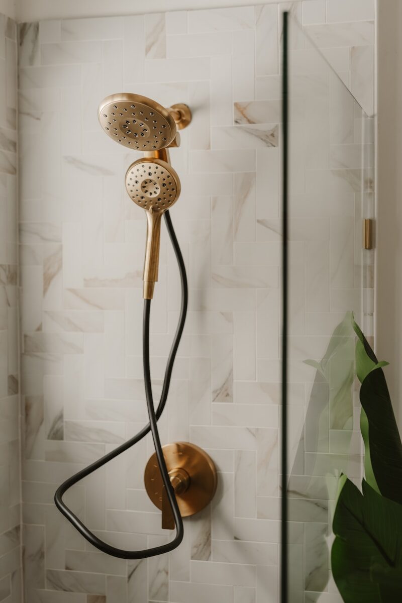 Gold shower head with black hose in modern bathroom.